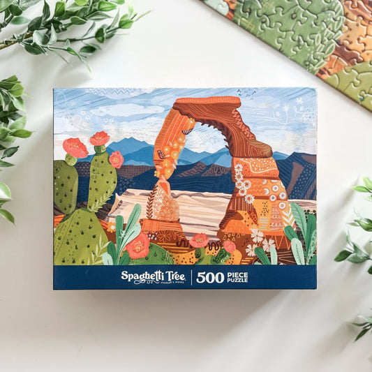 Spaghetti Tree puzzle box with desert-themed artwork on a white surface with greenery